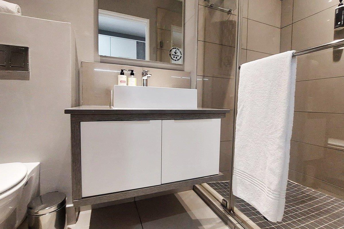 Modern bathroom featuring a floating vanity with vessel sink, wall-hung toilet, and a glass-enclosed shower with neutral wall tiling.