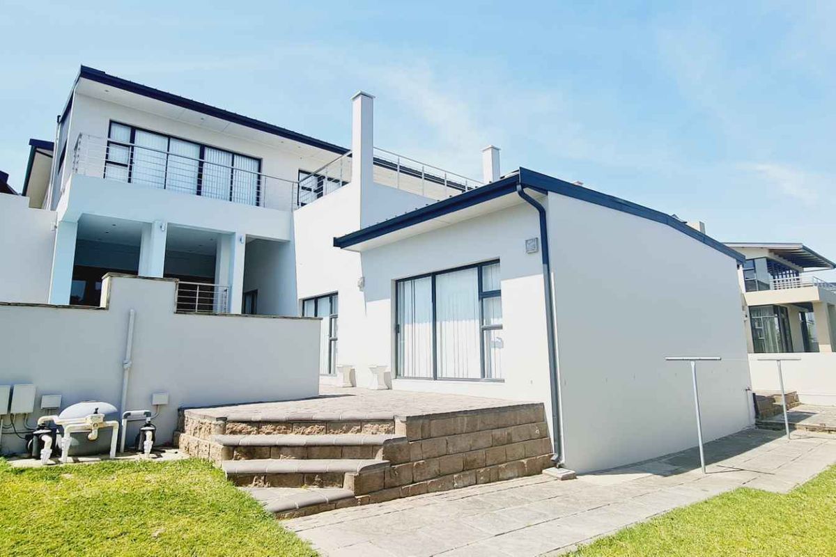 Rear view of a modern multi-level house featuring a paved patio, stone steps, and a balcony overlooking the garden area.