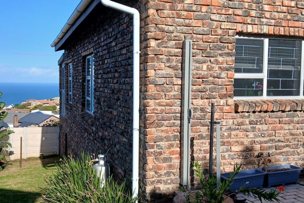 Exterior view of a face-brick house featuring security bars on windows, a gutter system, and a paved area with a coastal view.