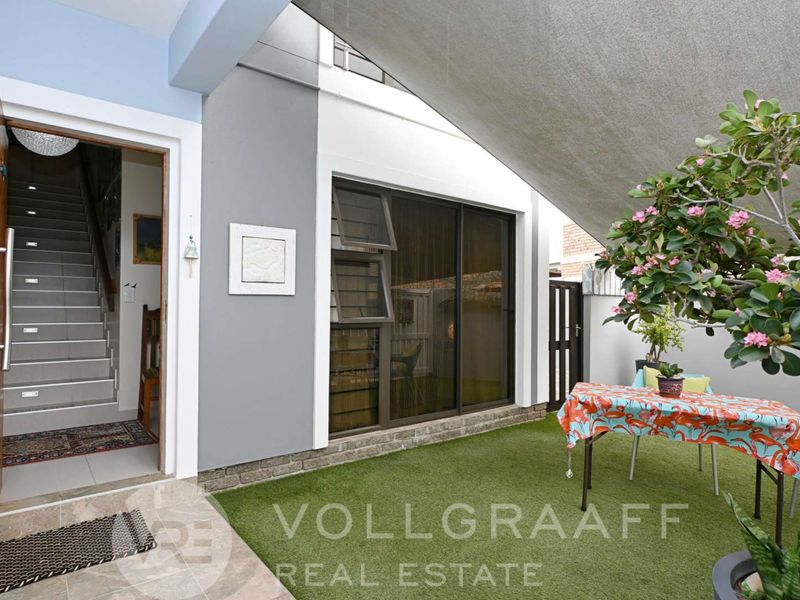 A covered patio area featuring artificial turf, a sliding glass door, and direct access to the home's interior staircase.