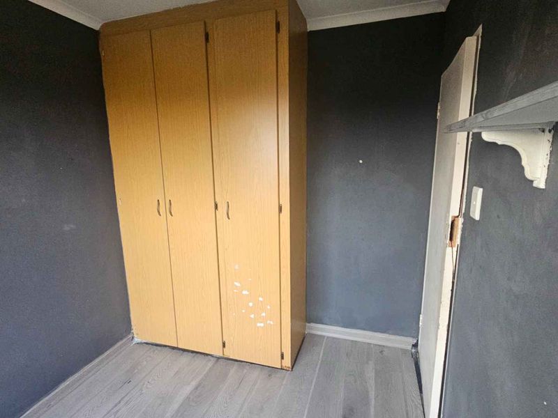 A compact bedroom featuring laminate flooring, dark-painted walls, and a built-in wooden wardrobe, offering a blank canvas for potential renovation or restyling.