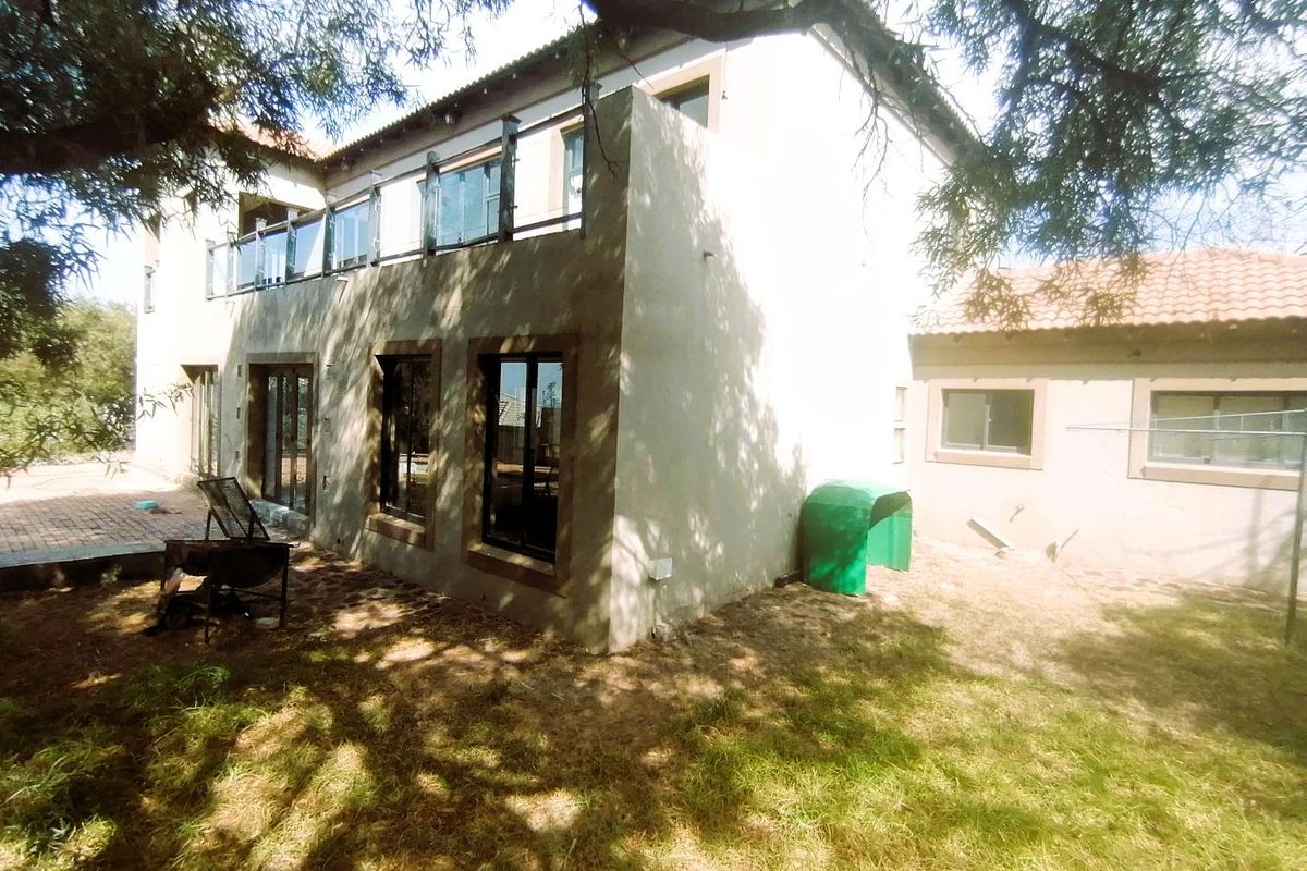 Rear view of the house featuring a balcony with glass balustrades, paved patio area, and unfinished exterior wall plastering.