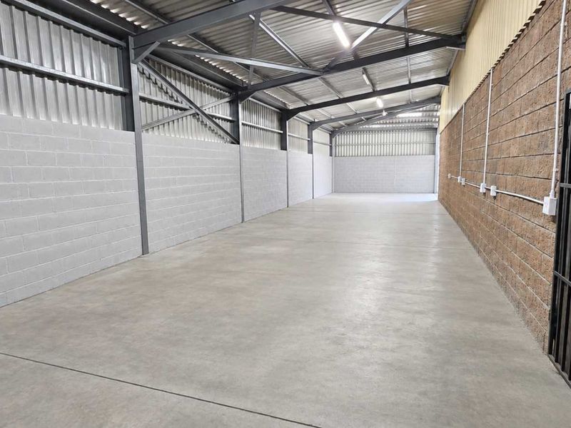 Spacious industrial utility area featuring a concrete floor, exposed steel roof trusses, and secure access gate, suitable for storage or workshop use.