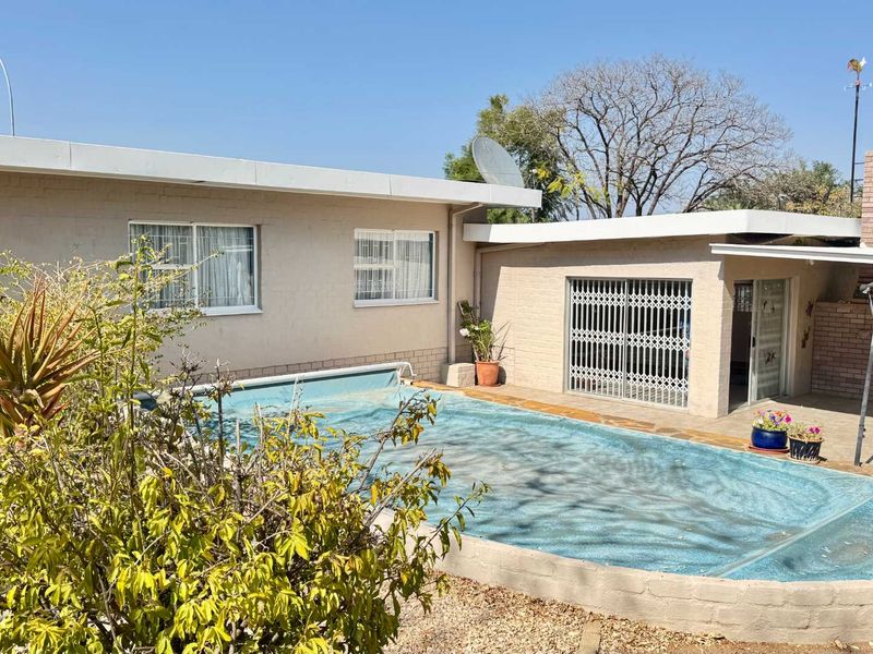 Rear exterior view featuring a swimming pool with cover, a covered patio area with a built-in brick fireplace, and secure access points.