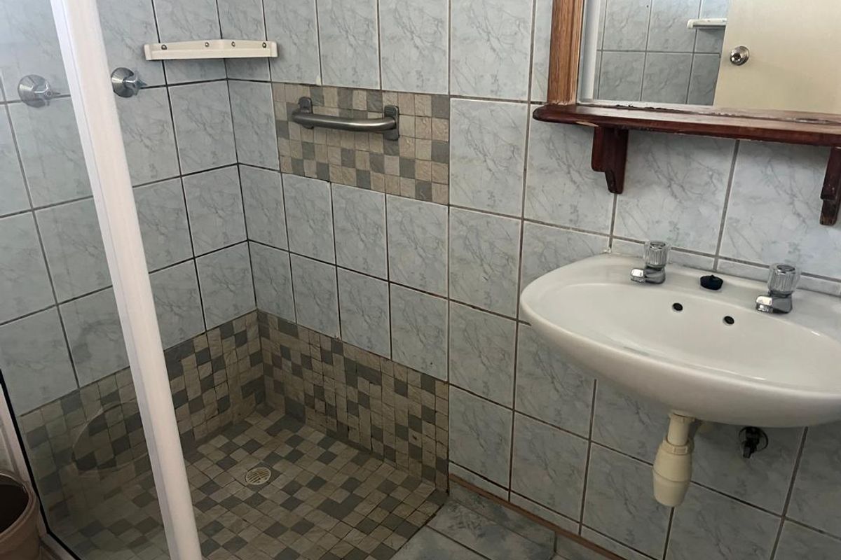 A functional bathroom featuring a tiled shower enclosure with grab rail, wall-mounted basin, and wooden-framed mirror.