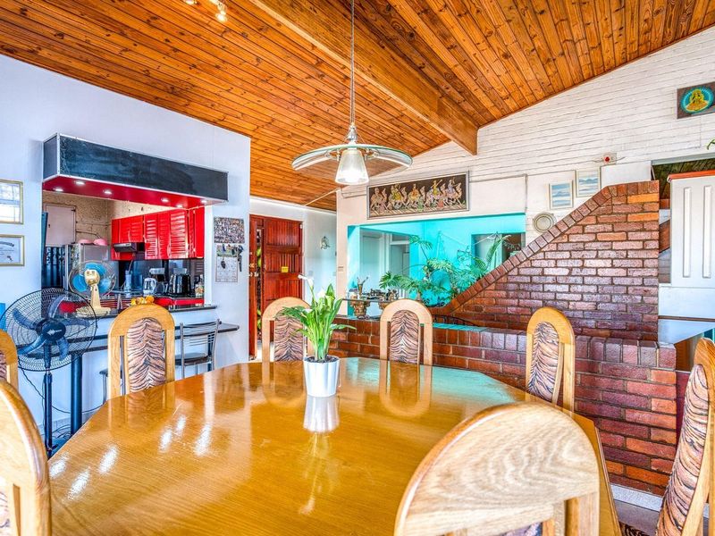 Open-plan living and dining area featuring a vaulted timber ceiling, exposed brickwork, and an integrated kitchen with red cabinetry.