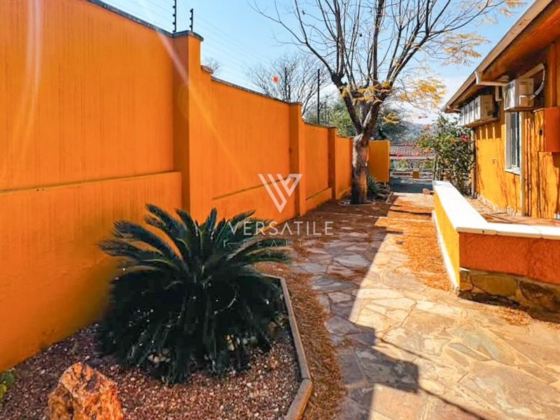 A side exterior walkway featuring a stone path, perimeter wall with electric fencing, and raised planter beds along the side of the house.