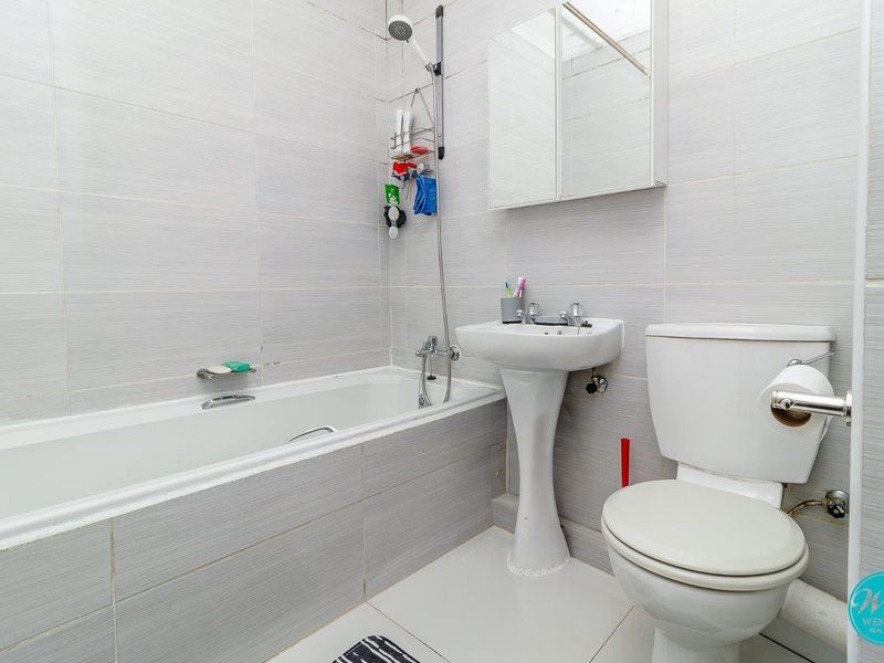 A functional bathroom featuring a bathtub with shower attachment, pedestal sink, toilet, and mirrored medicine cabinet, finished with neutral wall tiling.