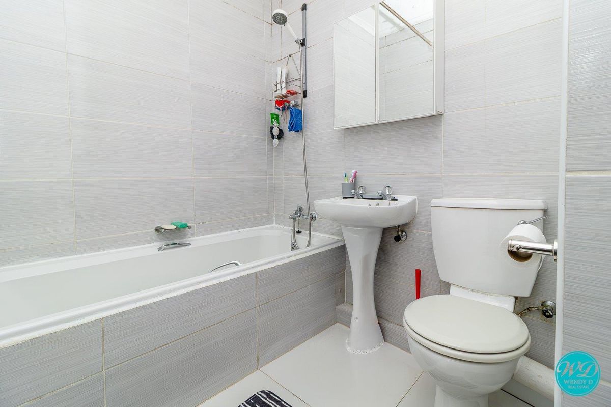 A functional bathroom featuring a bathtub with shower attachment, pedestal sink, toilet, and mirrored medicine cabinet, finished with neutral wall tiling.