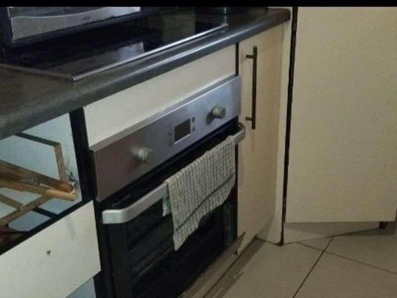 A kitchen area featuring a built-in oven, electric cooktop, and tiled flooring, currently showing signs of wear and missing cabinetry components.