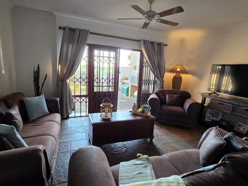 A comfortable living room featuring tiled flooring, a ceiling fan, and direct access to an outdoor patio through a secure sliding door.