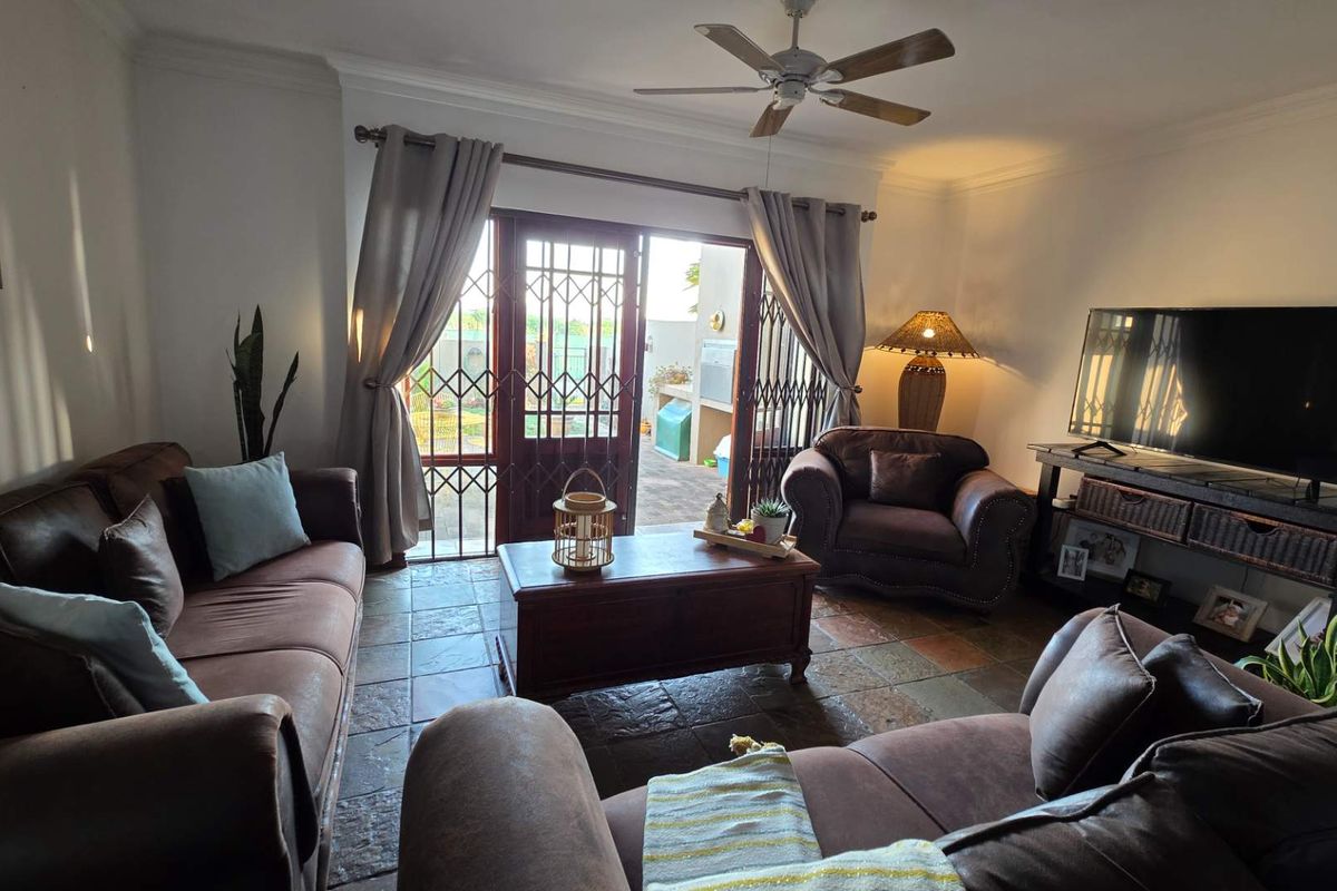 A comfortable living room featuring tiled flooring, a ceiling fan, and direct access to an outdoor patio through a secure sliding door.