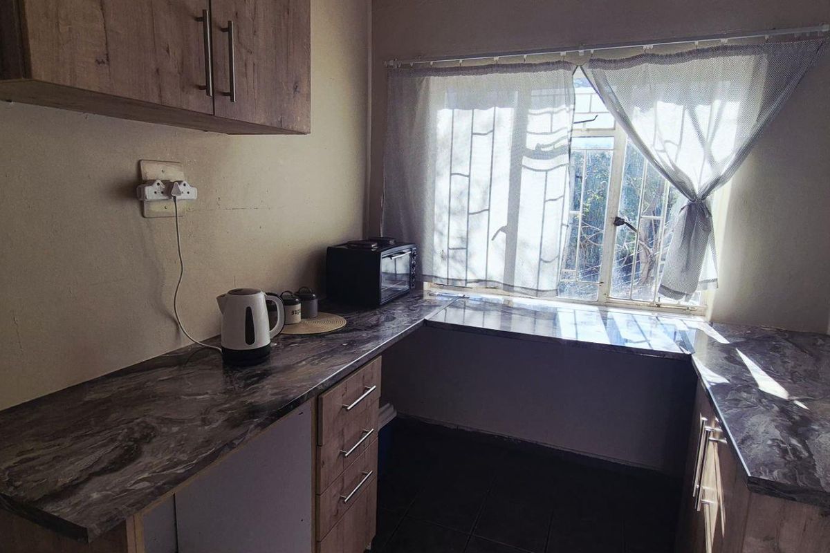 A functional kitchen featuring wood-look cabinetry, marble-effect laminate countertops, and a window with security bars.