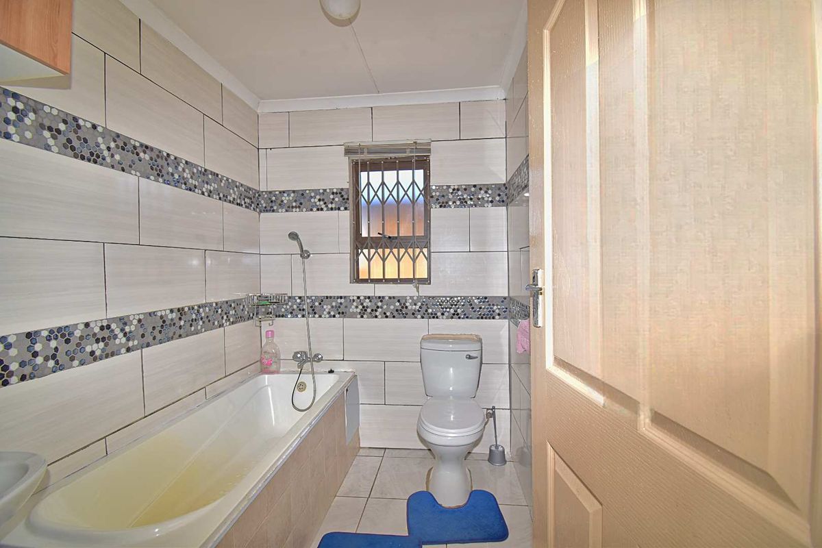 A functional bathroom featuring a bathtub with shower attachment, toilet, and decorative tiled walls with a mosaic accent border.