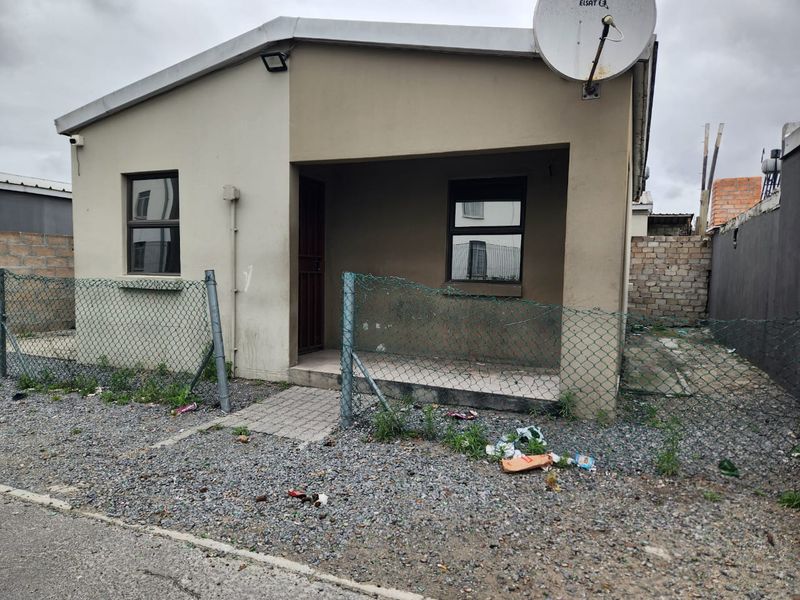 Front view of a detached house featuring a small covered entrance, security gate, and chain link perimeter fencing.