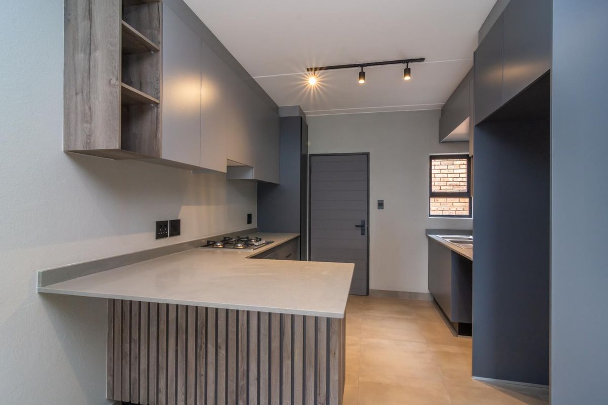 Modern kitchen featuring sleek grey cabinetry, stone countertops, a built-in gas hob, and contemporary track lighting.