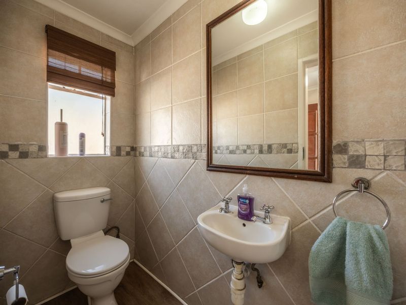 A compact guest bathroom featuring neutral ceramic wall tiles, a pedestal basin, and a dual flush toilet.