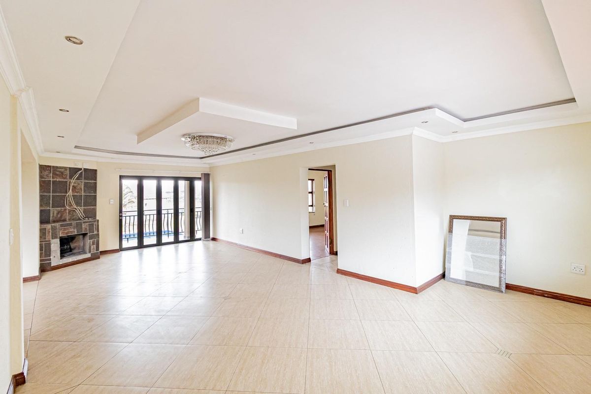 Spacious open-plan living area featuring tiled flooring, a built-in fireplace with stone cladding, recessed ceiling details, and large glass doors leading to a balcony.