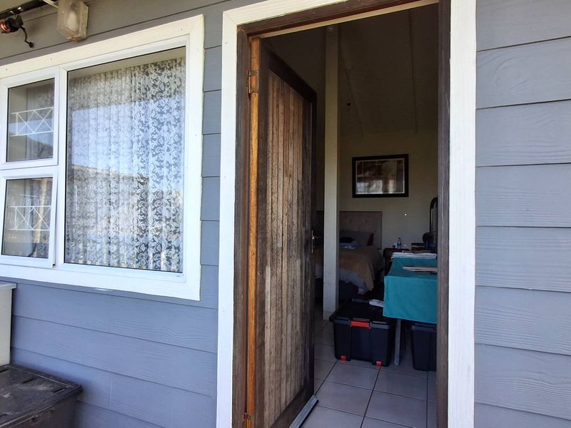 Exterior view of a building entrance featuring weatherboard cladding, a timber door, and a window, showing access into an interior living space.