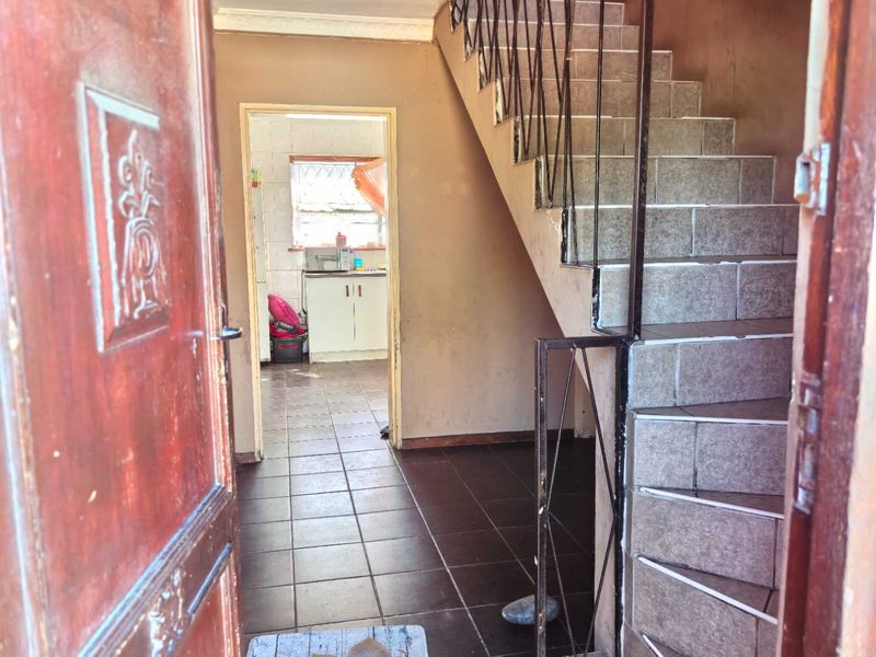Entrance area featuring a tiled staircase with metal balustrade, leading through to a kitchen space with tiled flooring.