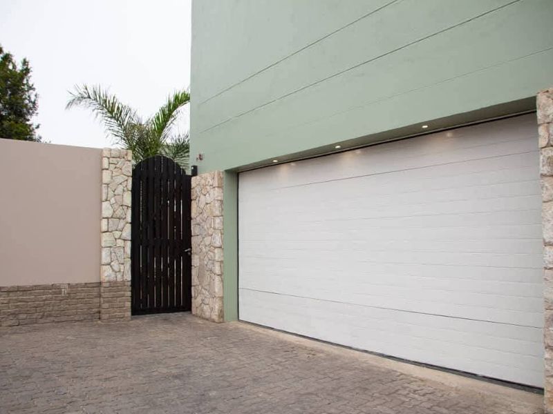 Modern garage exterior featuring a clean sectional door, stone-clad pillars, and a paved driveway with integrated recessed lighting.