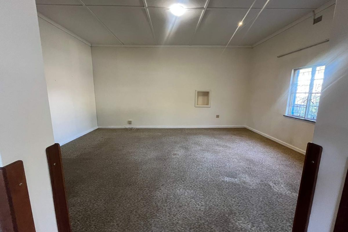 A spacious, empty living room featuring wall-to-wall carpeting, a recessed wall niche, and a window providing natural light.