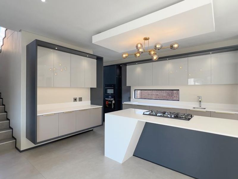 Modern kitchen featuring a central island with gas hob, sleek cabinetry, stone countertops, and an adjacent staircase in a contemporary open-plan layout.