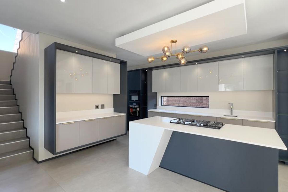 Modern kitchen featuring a central island with gas hob, sleek cabinetry, stone countertops, and an adjacent staircase in a contemporary open-plan layout.