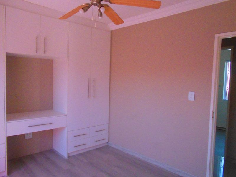 A clean bedroom featuring built-in cupboards, an integrated desk, laminate flooring, and a ceiling fan.