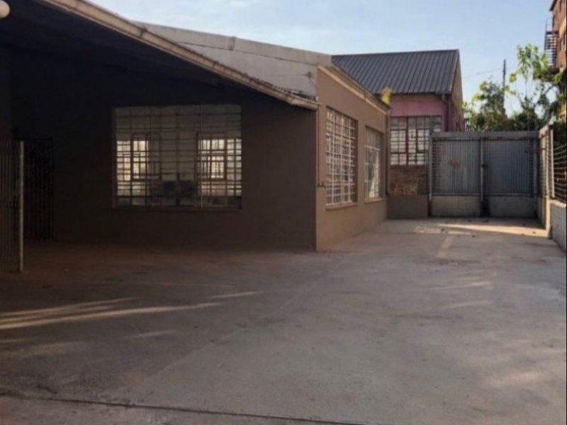 A functional industrial rear yard featuring a concrete surface, covered loading area, and secure window bars, suitable for storage or logistics operations.