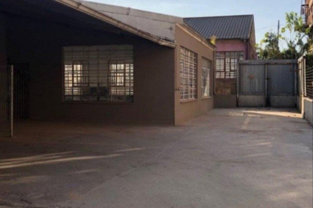 A functional industrial rear yard featuring a concrete surface, covered loading area, and secure window bars, suitable for storage or logistics operations.