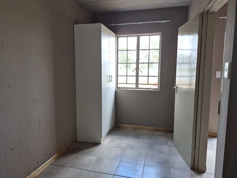 A compact bedroom featuring tiled flooring, a built-in wardrobe, and a window with security bars, currently in an unfinished state.