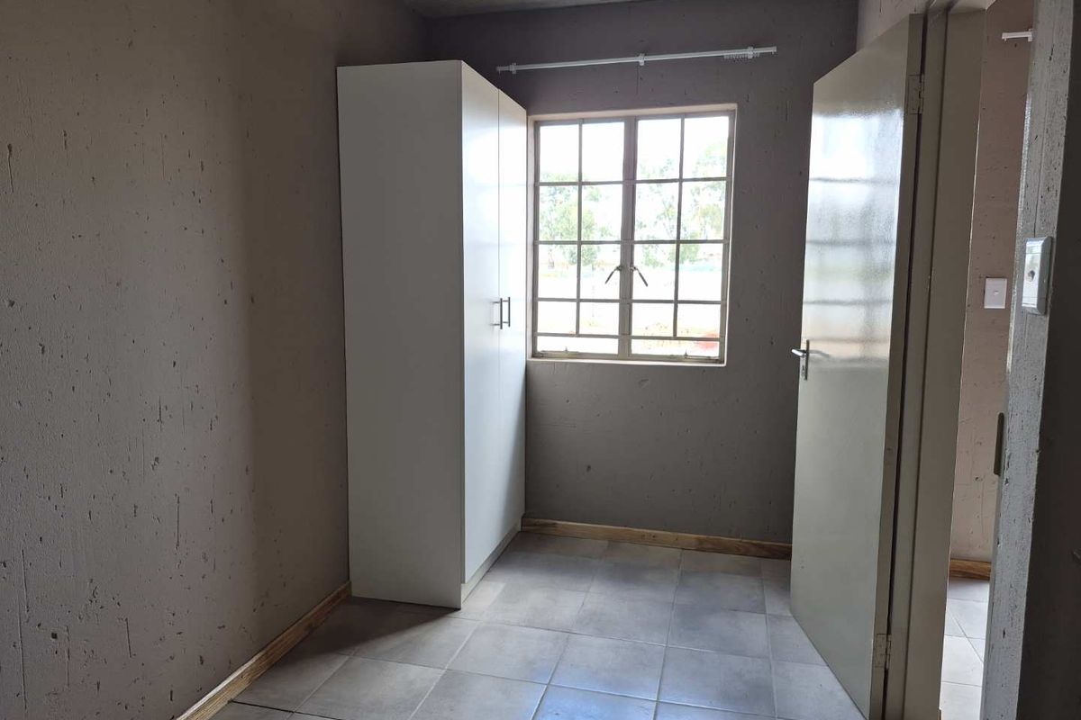 A compact bedroom featuring tiled flooring, a built-in wardrobe, and a window with security bars, currently in an unfinished state.