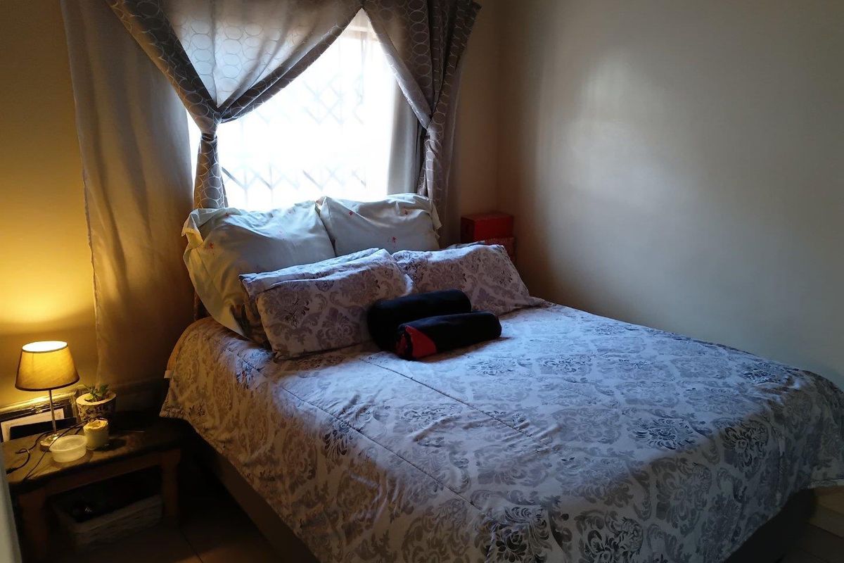A cozy bedroom featuring tiled flooring and a window fitted with a security gate, providing a functional and private sleeping space.