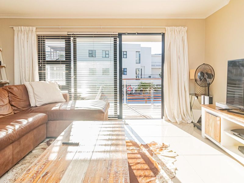 Bright living room featuring large sliding glass doors leading to a balcony, tiled flooring, and neutral wall finishes.