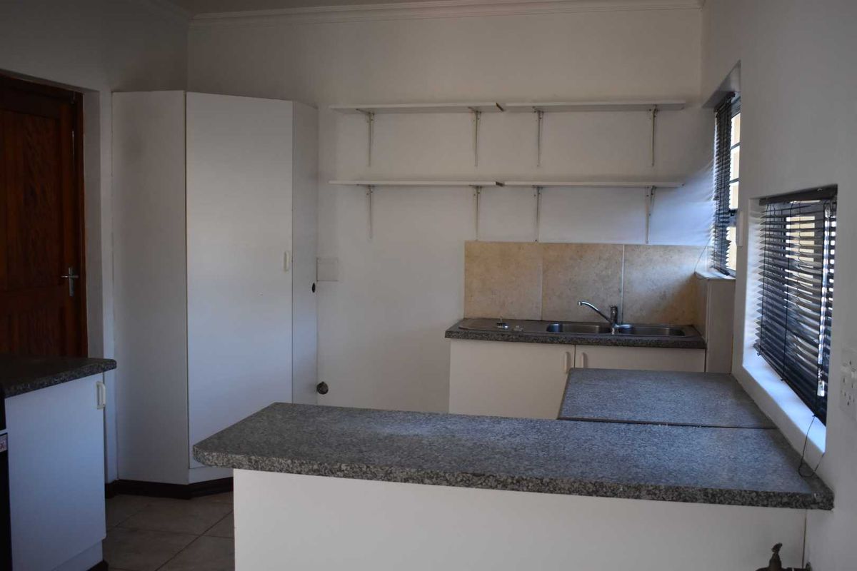 A functional kitchen area featuring granite-look countertops, a double sink, built-in cabinetry, and open wall shelving, offering a practical layout for daily use.