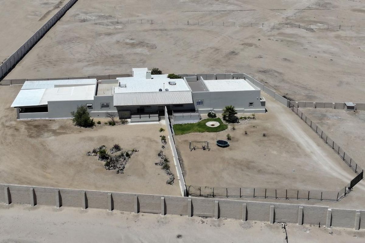Aerial view of a detached house situated on a large, expansive plot enclosed by a perimeter wall and fencing.