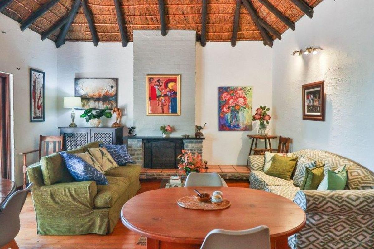 Spacious living area featuring a traditional thatched roof with exposed timber beams and a central brick fireplace.