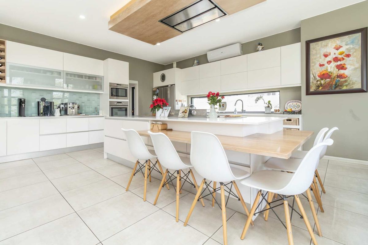 Modern kitchen featuring white cabinetry, integrated appliances, a central island with breakfast bar seating, and a sleek ceiling-mounted extractor fan.