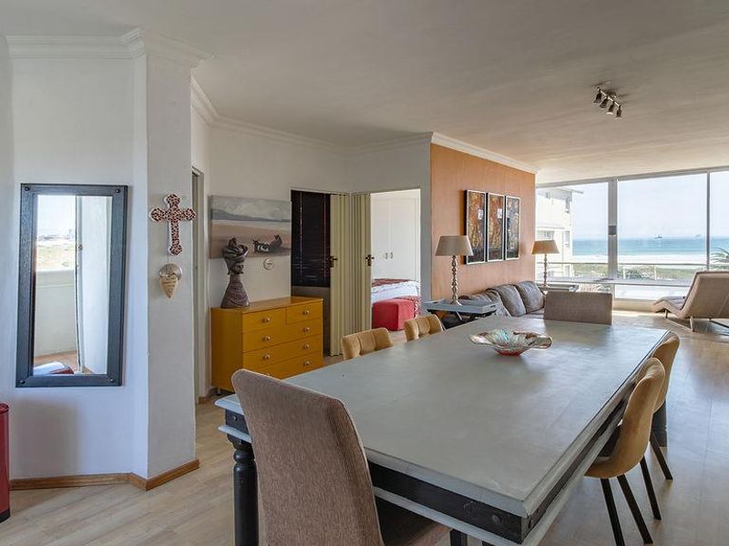 Spacious open-plan living and dining area featuring large windows with ocean views, laminate flooring, and direct access to an outdoor balcony.