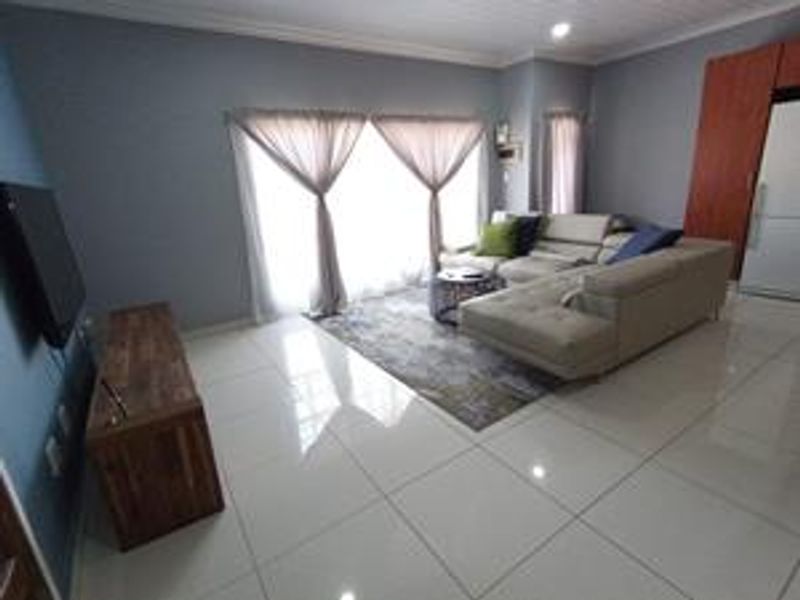 A well-maintained living room featuring polished tiled flooring, cove molding, and large sliding glass doors that provide ample natural light.