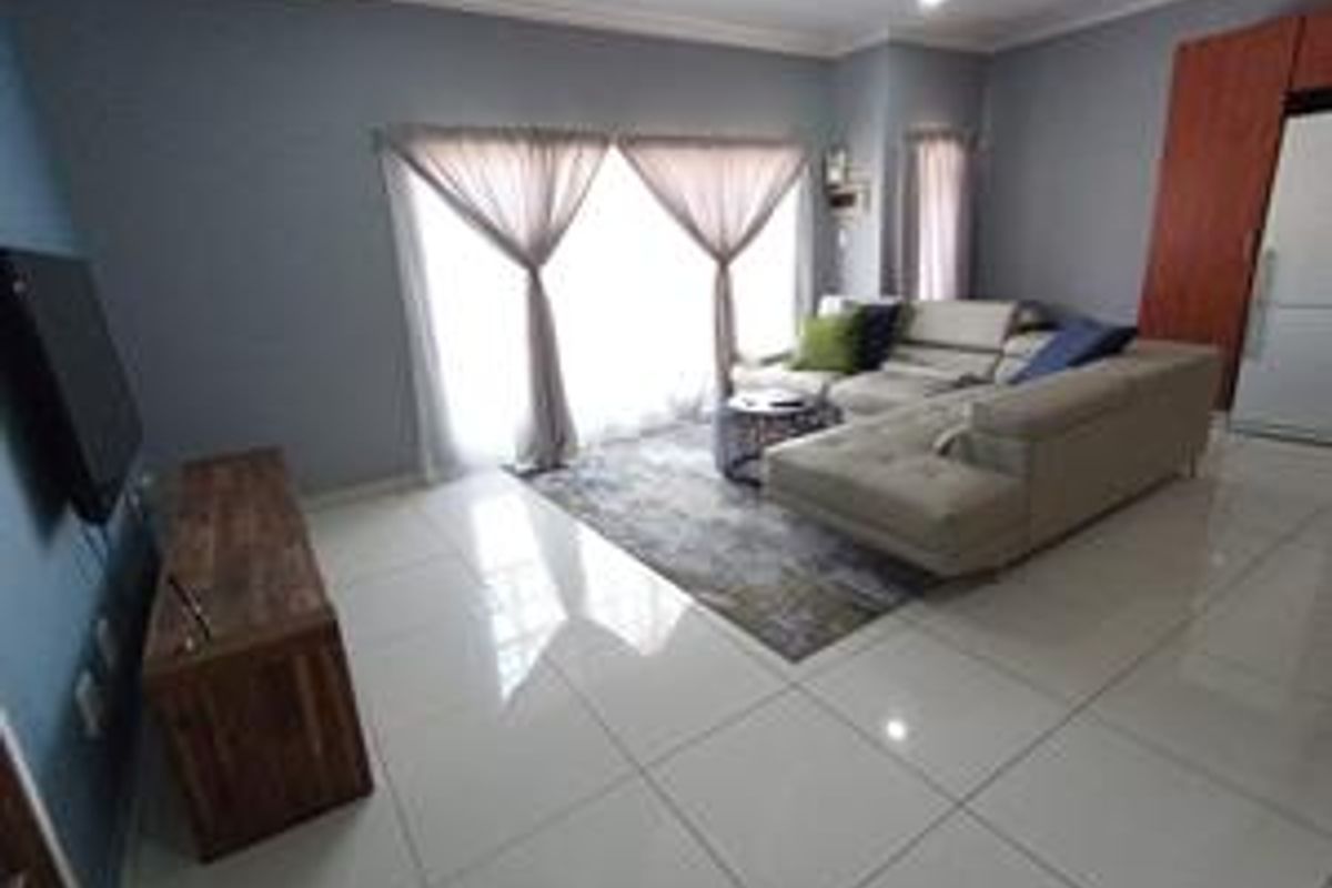 A well-maintained living room featuring polished tiled flooring, cove molding, and large sliding glass doors that provide ample natural light.