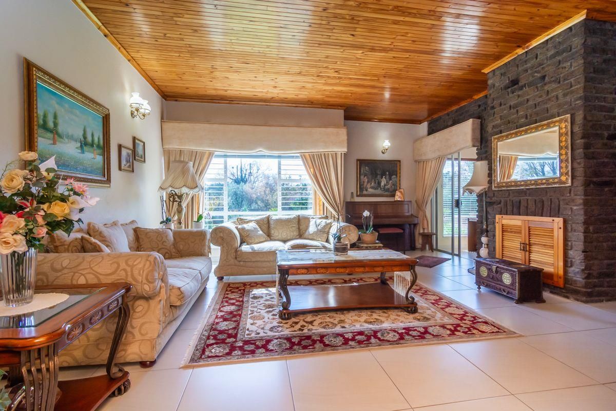 Spacious living room featuring a prominent dark brick fireplace, high timber-paneled ceilings, and large windows providing ample natural light.