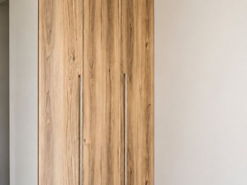 A clean, modern bedroom featuring neutral tiled flooring, a contemporary wood-finish built-in wardrobe, and a ceiling fan.