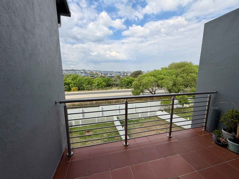 A private balcony featuring tiled flooring and a modern stainless steel balustrade, offering elevated views over the surrounding neighborhood and garden area.