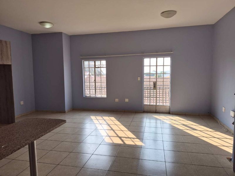 Spacious open-plan living area featuring neutral tiled flooring, ample natural light, and direct access to an outdoor balcony through a glass panel door.