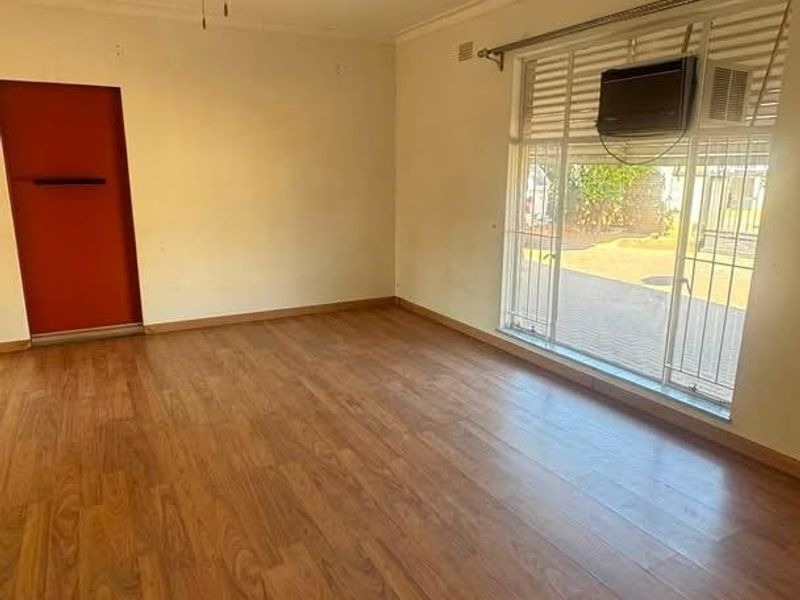 An empty living room featuring laminate flooring, a ceiling fan, and a window-mounted air conditioning unit with security bars.