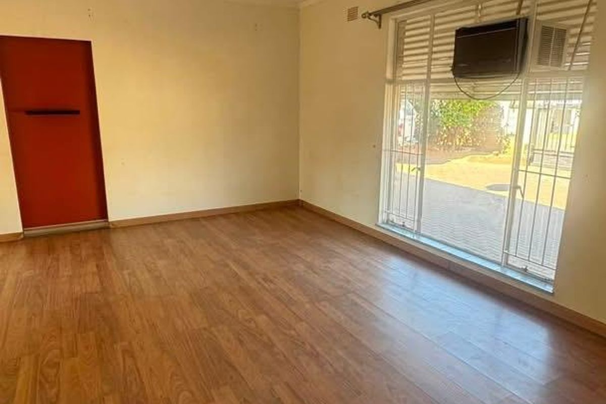 An empty living room featuring laminate flooring, a ceiling fan, and a window-mounted air conditioning unit with security bars.