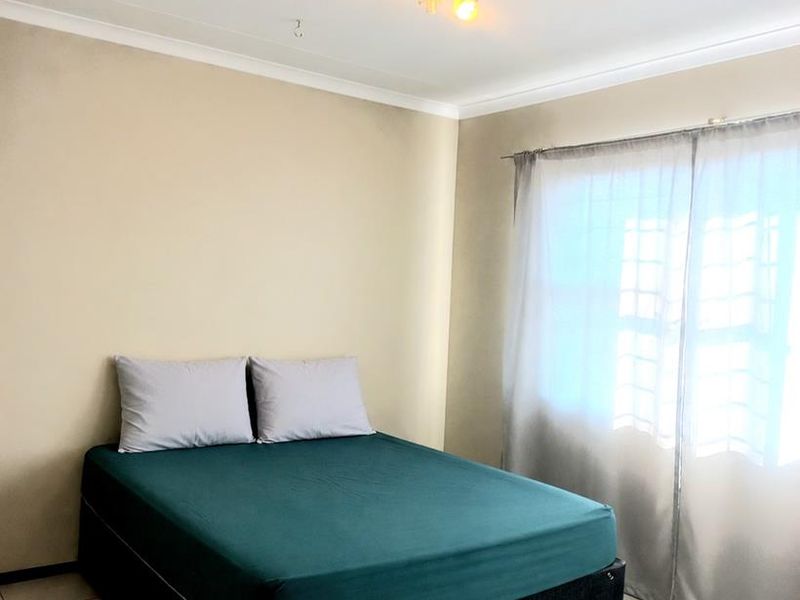A simple bedroom featuring tiled flooring, neutral walls, and a ceiling-mounted light fixture, offering a clean and functional space.