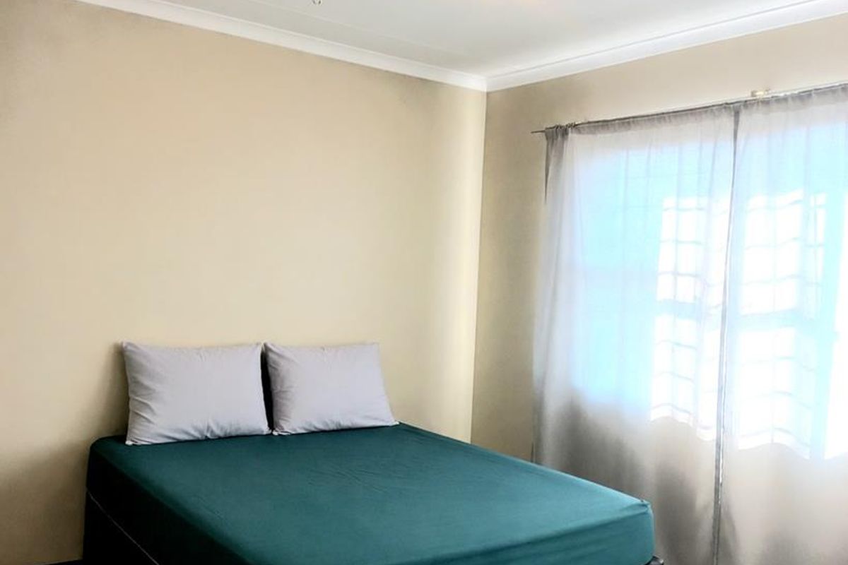 A simple bedroom featuring tiled flooring, neutral walls, and a ceiling-mounted light fixture, offering a clean and functional space.